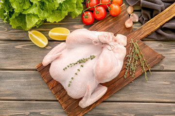 Wooden board with whole chicken and thyme on table