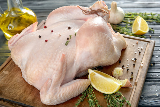 Fresh raw whole chicken with spices and lemon on wooden board