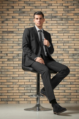 Handsome man in elegant suit sitting on chair near brick wall