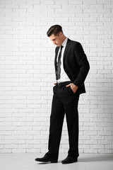 Handsome man in elegant suit near white brick wall