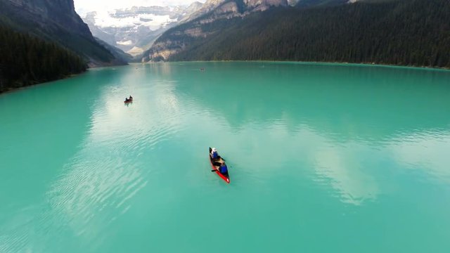 Aerial flythrough of beautiful emerald lake and mountains in Canada. People in a canoe and kayak