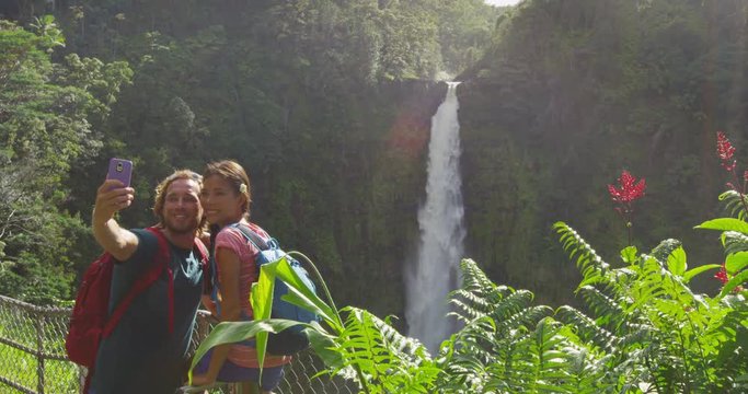 USA Hawaii couple tourists taking travel phone selfie self portrait with smartphone on Hawaii, Big Island, Akaka Falls. Happy cheerful young multicultural couple on travel. RED EPIC SLOW MOTION.