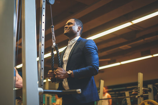 Exercise for triceps in the gym. African bussinesman in classic suit performs an exercise on the triceps in the simulator. fitness in gym.