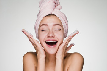 lovely laughing girl with a pink towel on her head applies cleansing foam on her face