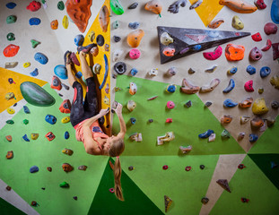Fototapeta premium Young woman bouldering in climbing gym, hanging in upside down position