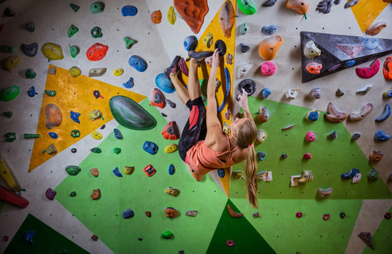 Young woman bouldering on overhanging wall in indoor climbing gym