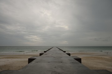 Fototapeta na wymiar Sandy beach, concrete pier, dramatic stormy sky, Florida Gulf Coast