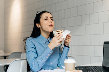 hungry young girl student in a blue shirt eagerly eats a sandwich in a cafe