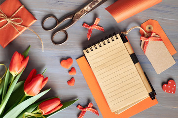 Blank notebook, wrapped gift, wrapping materials and fresh orange tulips on wooden table