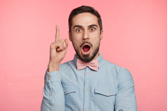 Shocked bearded man gets brilliant thought in mind, raises fore finger with clever expression, isolated over pink background. Successful businessman realizes his fault or mistake in business plan