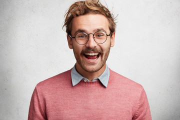 Content satisfied glad male dressed in pink sweater with shirt and spectacles has happy smile on...
