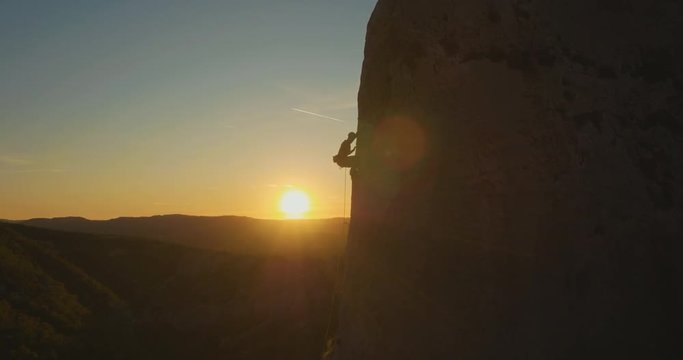 Aerial fly-by a man rock climbing outdoors at amazing sunset.
