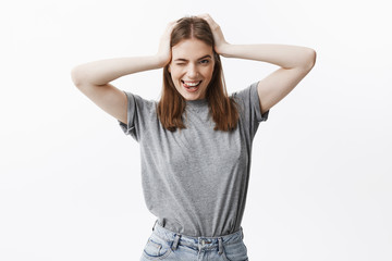 Fototapeta premium Young beautiful caucasian female student with dark hair and brown eyes in casual grey clothes, winking, smiling with teeth and showing tongue, looking in camera being happy.