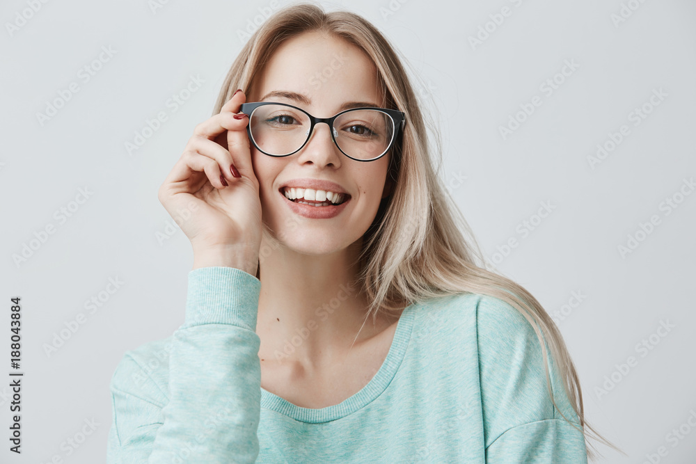 Wall mural Cheerful female student in stylish eyewear rejoices successfully passed exams, glad to have meeting with groupmates. Delighted beautiful pleased woman has attractive look, poses indoors.