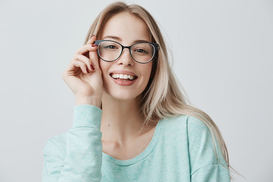 Cheerful female student in stylish eyewear rejoices successfully passed exams, glad to have meeting with groupmates. Delighted beautiful pleased woman has attractive look, poses indoors.