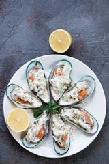White plate with green mussels baked in cheese sauce, gray asphalt background, view from above with space