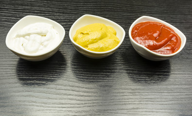 Garlic sauce, mustard and ketchup in bowls on a wooden table.