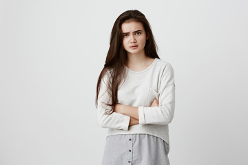 Indoor shot of dissatisfied offended beautiful young brunette dressed casually keeping arms folded, looking at camera with strict and skeptical expression, doesn't believe in excuses of boyfriend