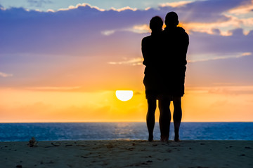 Silhouette eines Paares am Strand schaut sich gemeinsam den Sonnenaufgang über dem Meer im Urlaub...
