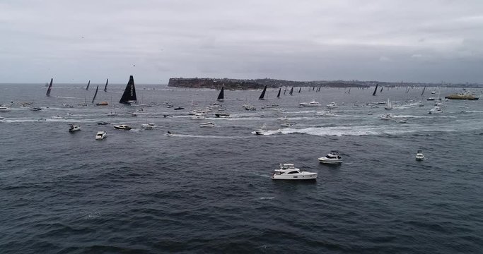 International super maxi yacht race from Sydney to Hobart at exit from Sydney Harbour surrounded by boats of spectators.
