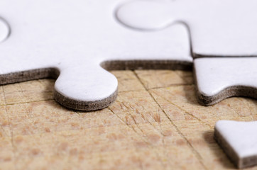 close up of a white jigsaw/puzzle with one gap, over wooden table background, symbol of problem...