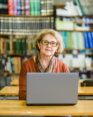 Serious senior woman using laptop in library