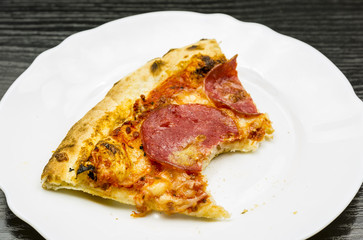 A bitten portion of pepperoni pizza on a plate.