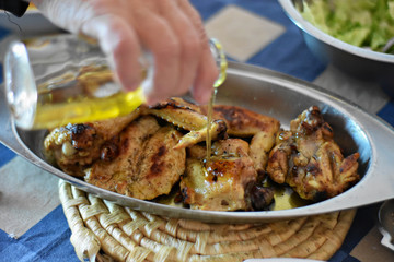 Woman pouring olive oil in grilled chicken meat