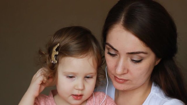 Mother and daughter in headphones look at the screen of the smartphone. Mom and child communicate by video link.