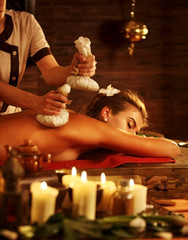 Massage of woman in spa salon. Girl on candles background in spa salon. Luxary interior in oriental therapy salon. Different types of relaxation. Close up of female hands give herbs hot ball therapy.
