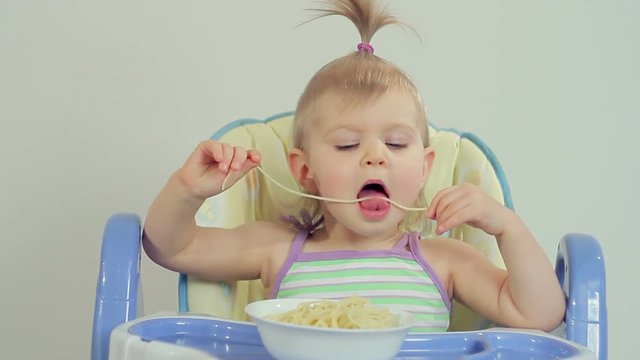 Charming little girl eating spaghetti with her fingers and enjoying it