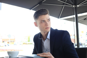 Portrait of a confident businessman sitting on the bench and drinking coffee outdoors.