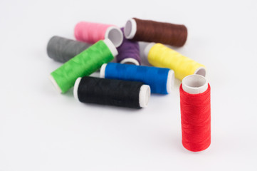 One red bobbin of thread near heap of bobbins of new colorful threads on white background