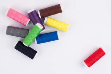 One red bobbin of thread near heap of bobbins of new colorful threads on white background. Top view