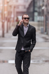 Young entrepreneur businessman walking, talking on his smart phone and smiling, outdoors in the streets