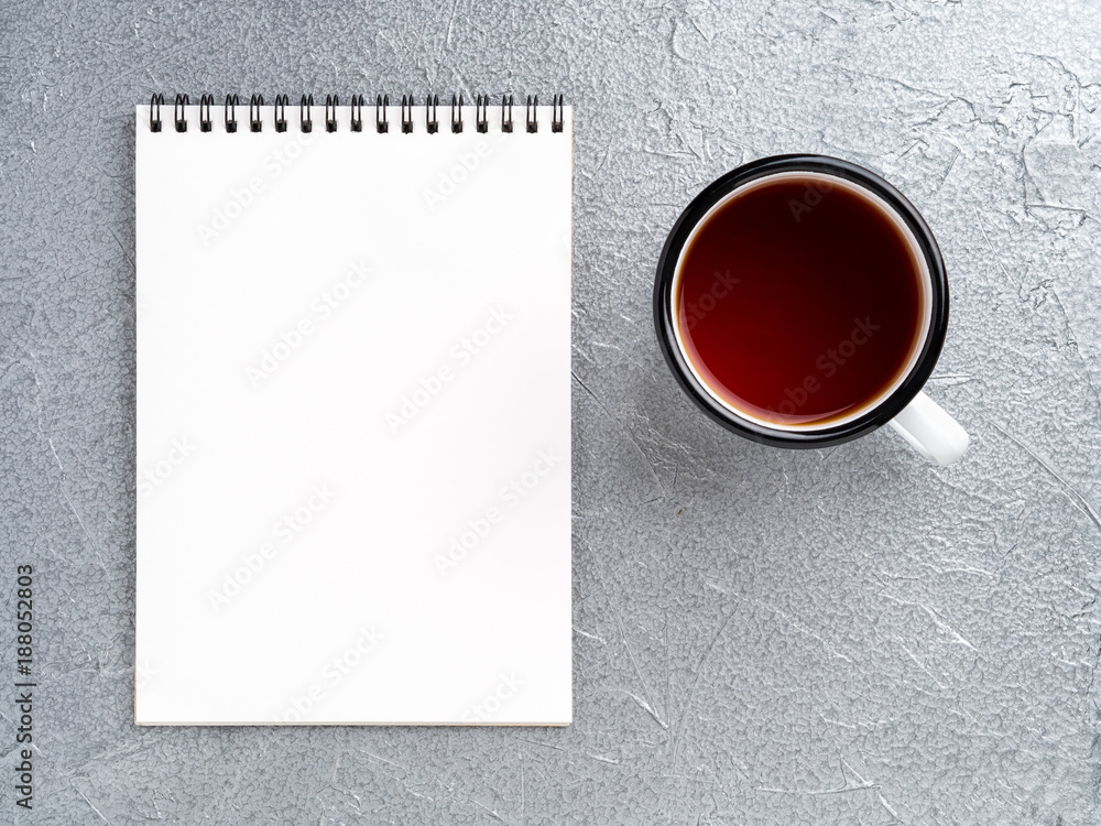 Wall mural metal mug with tea, empty a blank sheet of notepad on the spiral on a gray metallic background