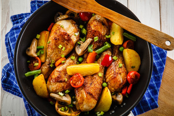 Grilled chicken drumsticks with vegetables on wooden background