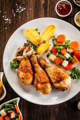 Grilled chicken drumsticks with vegetables on wooden background