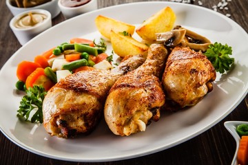 Grilled chicken drumsticks with vegetables on wooden background