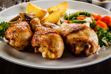 Grilled chicken drumsticks with vegetables on wooden background