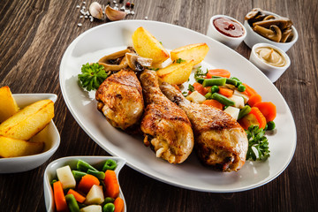 Grilled chicken drumsticks with vegetables on wooden background