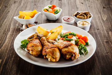 Grilled chicken drumsticks with vegetables on wooden background