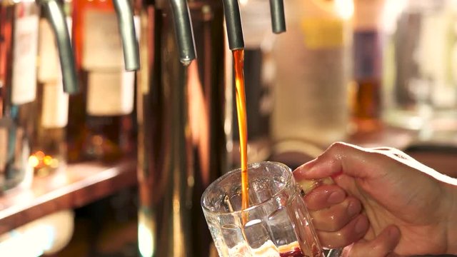 Dark beer filling and overflowing. Bartender pouring dark craft beer from tap into pint glass.