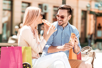 Couple eating sandwich and talking outdoor in city after shopping.