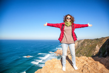 a young beautiful woman spread her arms and embraces the whole world, against the backdrop of Cape Cabo da Roca, Portugal, the Atlantic Coast. Freedom, youth, travel