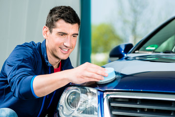 Young man using an absorbent soft towel for drying and polishing the surface of a clean blue car