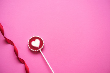 Pink Valentine's day heart shape lollipop candy on empty pink paper background. St. Valentine's Day or Anniversary concept.