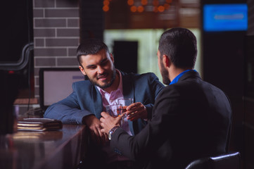 Two young businessmen in formal suits met in bar at an informal meeting and drink whiskey