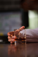 Close-up - the hand of young unidentified man holding glass of whiskey on bar stand