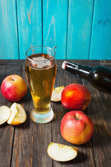 Glass of cider with apples and bottle on rustic wooden background
